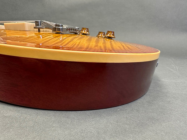 Close-up side view of electric guitar with sunburst finish and cream binding on body edge, showing bridge and control knobs on a grey background.