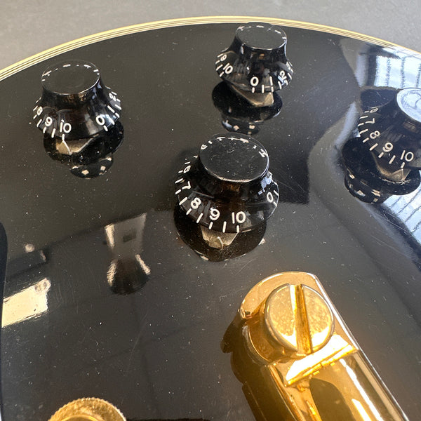 Close-up of black electric guitar control knobs and gold bridge hardware on glossy black body