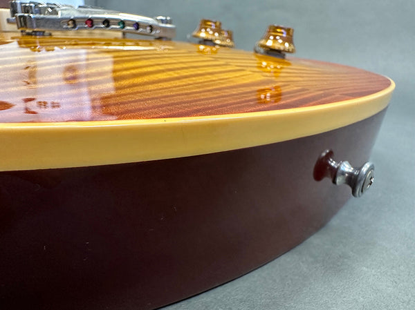 Close-up of electric guitar body showing sunburst finish, cream binding, and strap button on dark brown side panel
