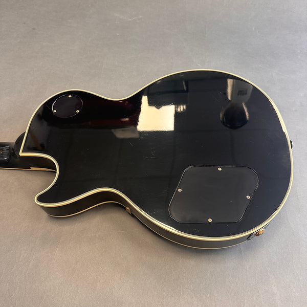 Back view of black electric guitar body with cream binding and two black control cavity covers on gray background