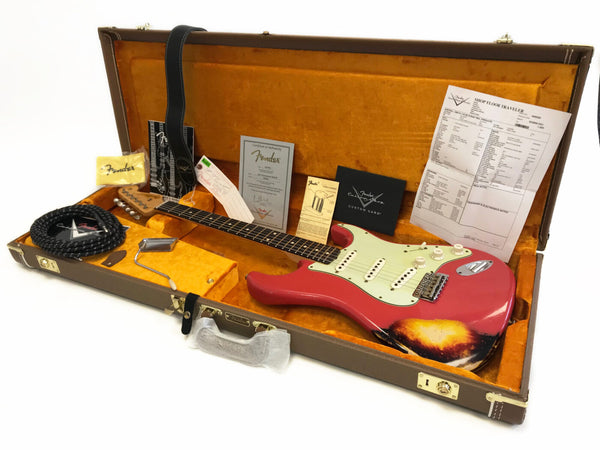 Fender Custom Shop electric guitar in red finish with vintage wear, displayed inside orange plush-lined hard case with Fender certificate of authenticity, guitar strap, tremolo arm, instrument cable, and documentation