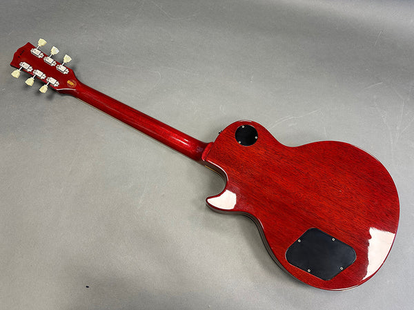 Back view of a glossy red solid body electric guitar with a set neck and chrome tuning pegs on a gray background