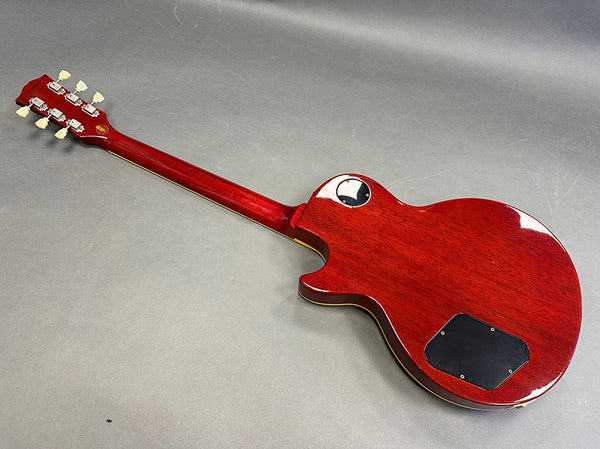 Back view of a cherry red electric guitar with a solid body and mahogany neck, featuring cream tuning pegs and black plastic control cavity covers.