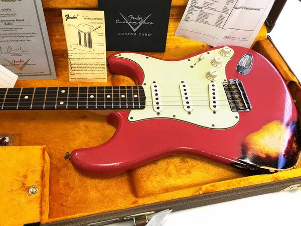 1963 Fender Stratocaster Relic electric guitar in fiesta red with three single-coil pickups, white pickguard, and rosewood fingerboard, displayed in a vintage orange plush-lined hard case with Fender Custom Shop certificate and tremolo springs instruction sheet.