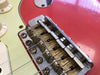 Close-up of vintage Fender electric guitar bridge and saddles on red body with white control knobs and pickguard