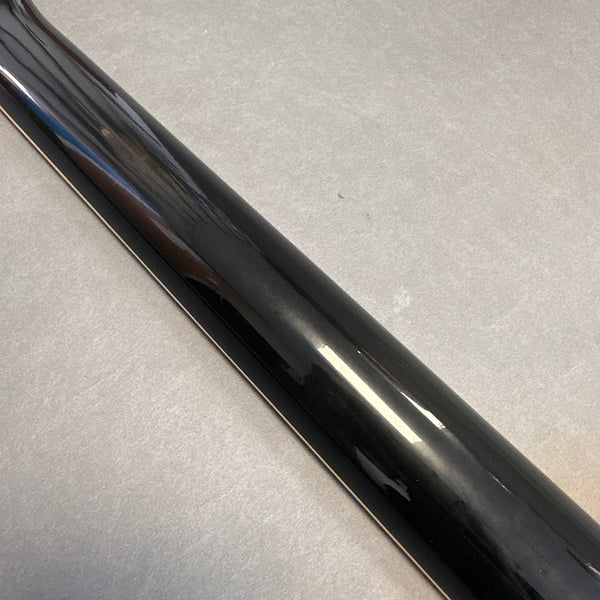 Close-up of glossy black guitar neck on a gray surface showing smooth finish and reflection.