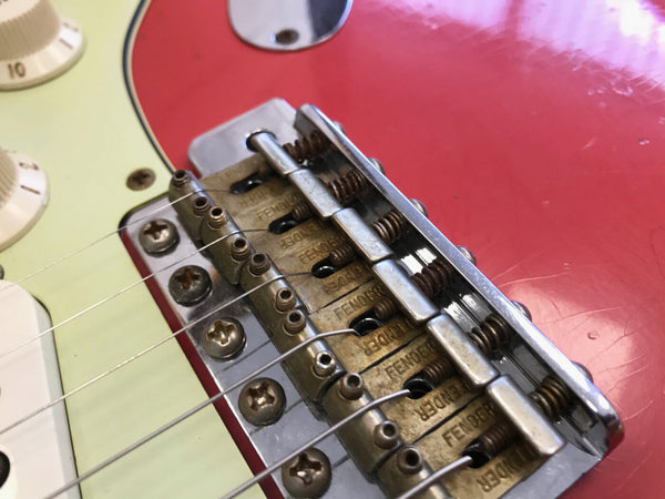 Close-up of vintage Fender electric guitar bridge and saddles on red body with white control knobs and pickguard
