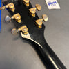 Close-up of black Gibson electric guitar headstock with gold and silver tuning pegs and Gibson USA tag on gray background