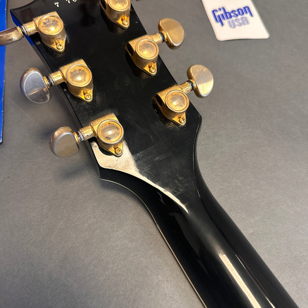 Close-up of black Gibson electric guitar headstock with gold and silver tuning pegs and Gibson USA tag on gray background