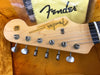 Close-up of Fender Stratocaster guitar headstock with tuning pegs and strings in orange plush guitar case