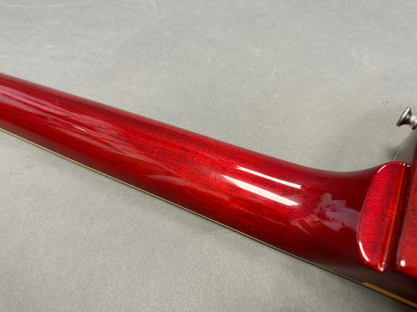 Close-up of glossy red wood guitar neck with visible grain and smooth finish on gray background