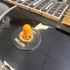 Close-up of black electric guitar toggle switch with yellow tip labeled Rhythm and Treble near fretboard and gold pickup ring