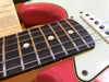 Close-up view of electric guitar fretboard with metal frets, dot inlays, and white pickguard on red guitar body