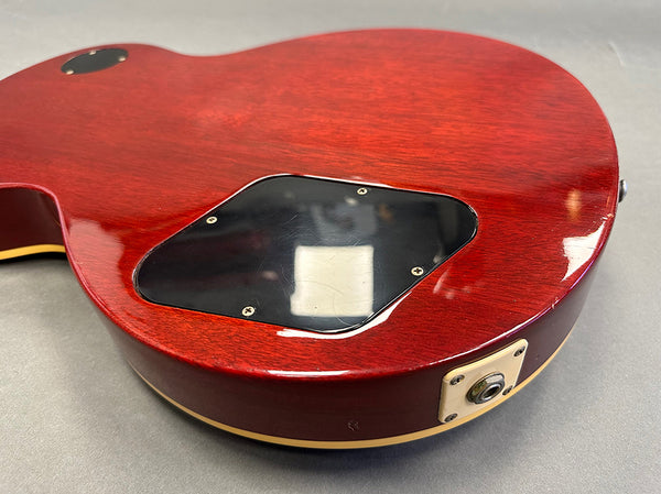 Close-up of the back of a red electric guitar body showing the control cavity cover and jack plate on a gray surface.