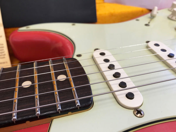 Close-up of electric guitar strings, pickups, and fretboard with dot inlays on a light-colored body with red accents at Coffee House Guitars.