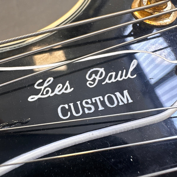 Close-up of black Les Paul Custom guitar headstock with white logo and strings.
