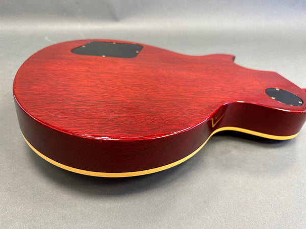 Close-up of the back of a red electric guitar body with cream binding and black control cavity covers on a gray surface