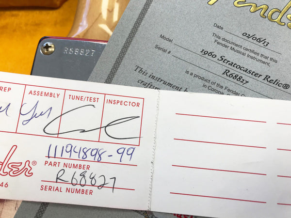 Close-up of Fender certificate and inspection tag for 1960 Stratocaster Relic guitar with serial number R68827, showing Fender quality control signatures and part number.