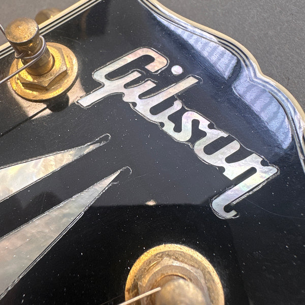 Close-up of Gibson guitar headstock with mother-of-pearl inlay and gold tuning pegs on black finish