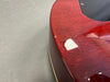 Close-up of red glossy guitar body showing wood grain and minor surface scratches next to black plastic plate