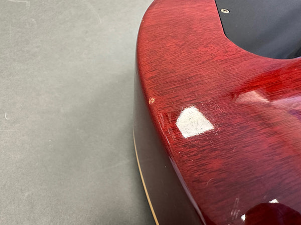 Close-up of red glossy guitar body showing wood grain and minor surface scratches next to black plastic plate