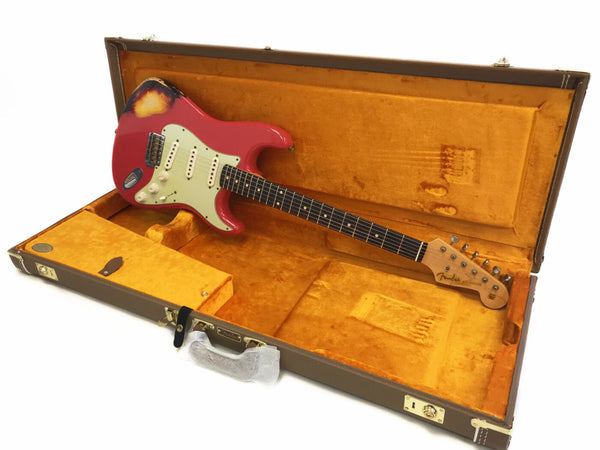 Fender Stratocaster electric guitar in red with vintage wear and three single-coil pickups, displayed inside open brown and orange plush-lined hard case