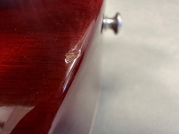 Close-up of minor chip damage on the red wooden body edge of a guitar with a strap button visible in the background