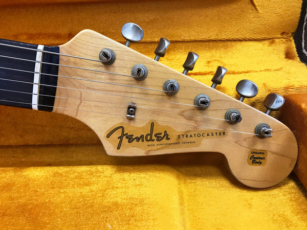 Close-up of Fender Stratocaster guitar headstock with tuning pegs and logo on natural wood finish, placed on yellow plush case interior