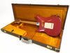 Vintage red electric guitar with worn finish in open brown hard case with orange interior lining