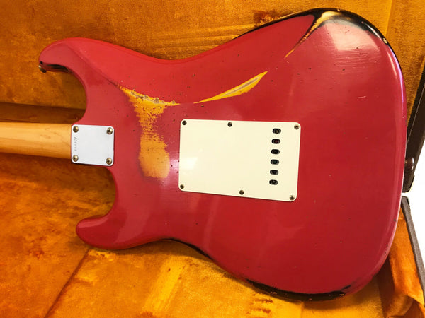 Red vintage electric guitar body with worn paint and white backplate resting on orange velvet case interior