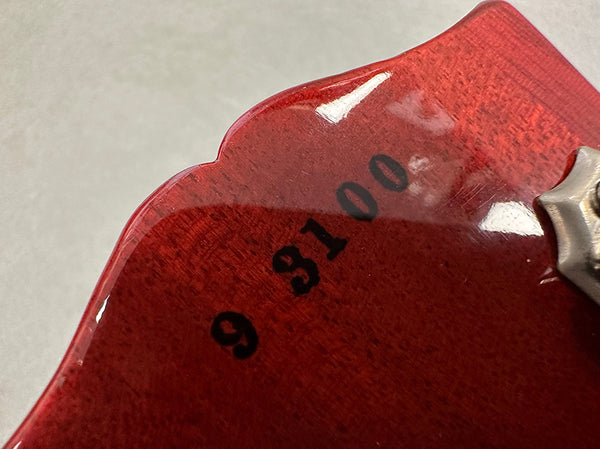 Close-up of red guitar headstock showing serial number 93100 stamped on wood near tuning peg.