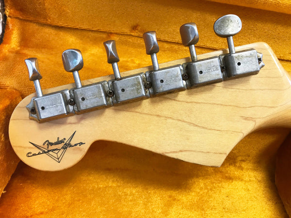 Close-up of vintage Fender Custom Shop guitar headstock with six chrome tuning pegs on natural maple wood background inside orange guitar case lining