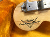 Close-up of Fender Custom Shop logo on the wooden part of a guitar inside a yellow plush-lined case