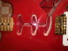 Close-up of red electric guitar body showing the empty pickup cavities, gold Fender bridge, and part of the neck with a quilted maple fretboard.