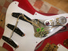 Close-up of red electric guitar with white pickguard removed, showing internal wiring, three single-coil pickups, potentiometers, and capacitor components