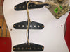 Close-up of vintage single-coil guitar pickups mounted on a white pickguard with exposed wiring and control plate.