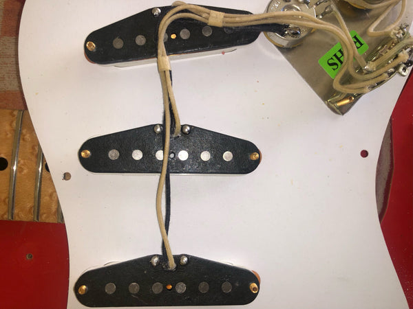 Close-up of vintage single-coil guitar pickups mounted on a white pickguard with exposed wiring and control plate.