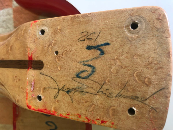 Close-up of a guitar neck heel with natural wood grain, signature, handwritten numbers, and red paint marks, featuring drilled holes for mounting.