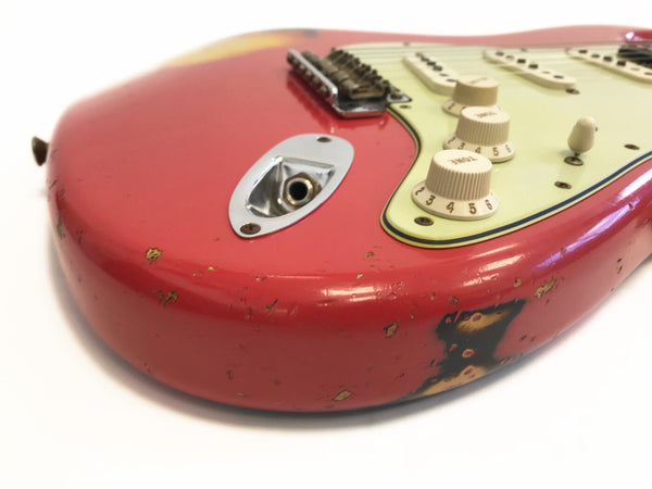 Close-up of worn red electric guitar body with cream control knobs and pickguard, showing vintage wear and scratches near input jack and bridge.