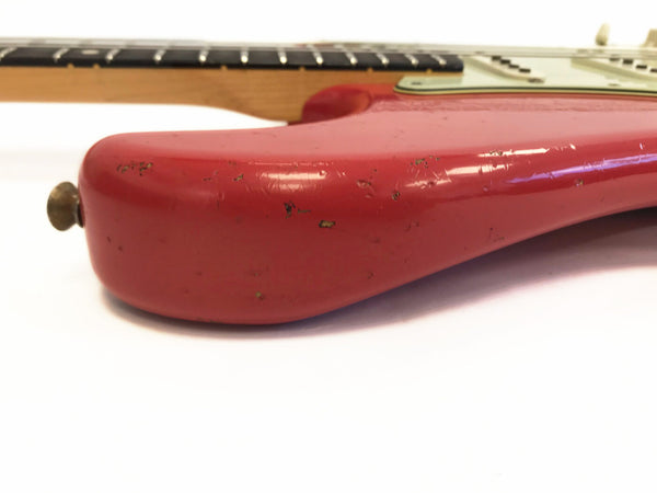 Close-up of red electric guitar body showing worn finish and scratches, partial view of maple neck and fretboard on white background