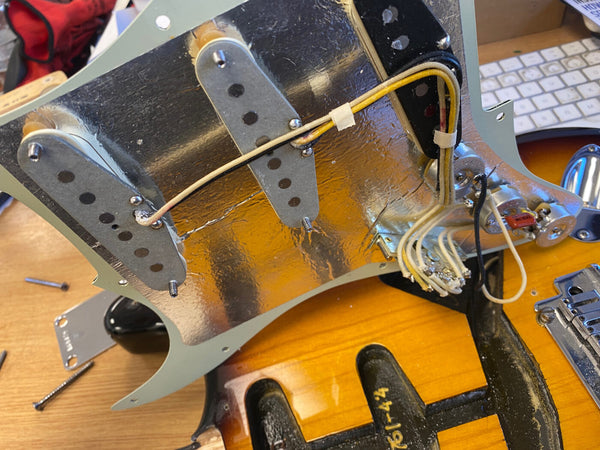 Close-up of vintage guitar pickguard with three single-coil pickups and internal wiring showing shielding foil and electronic components on a sunburst electric guitar body.