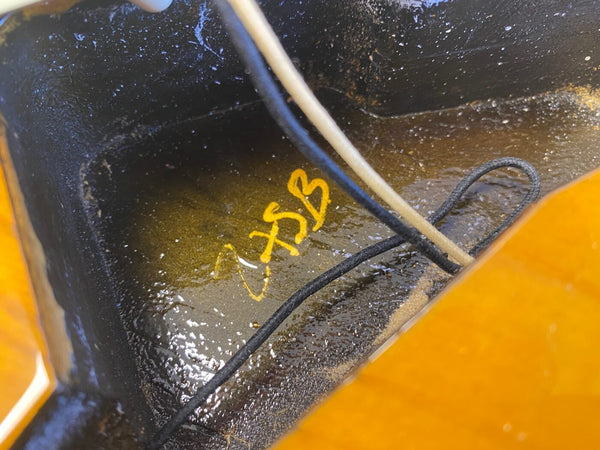 Close-up of inside electric guitar cavity showing wiring and handwritten yellow markings on black painted surface