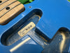 Close-up of vintage Fender guitar body cavity showing blue finish, serial number sticker, and part of maple fretboard with black dot inlays and metal strings.