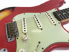 Close-up of red electric guitar body with white pickguard, three single-coil pickups, volume and tone knobs, and metal bridge with vintage-style saddles.