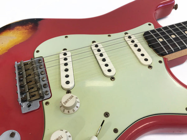 Close-up of red electric guitar body with white pickguard, three single-coil pickups, volume and tone knobs, and metal bridge with vintage-style saddles.