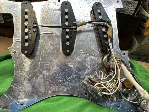 Close-up of vintage guitar pickguard with three single-coil pickups and wiring for electric guitar electronics, showing potentiometers and capacitor components.