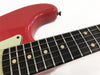 Close-up of red electric guitar body and black fretboard with metal frets and dot inlays against white background