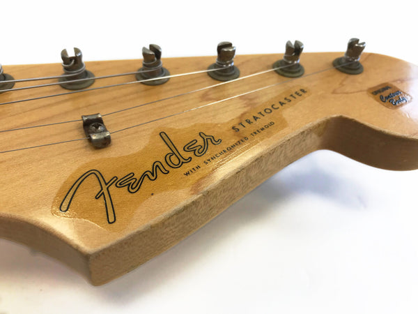 Close-up of Fender Stratocaster guitar headstock with tuning pegs and vintage logo on natural wood finish
