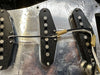 Close-up of vintage single-coil guitar pickups wired on metallic baseplate, showing model numbers and white and black connecting wires for electric guitar sound.