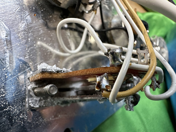 Close-up of internal wiring and soldering on electric guitar control plate showing white and yellow wires connected to metal terminals and a brown circuit board.
